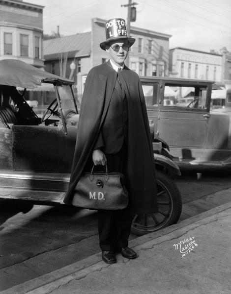 Man in a tophat, suit, and cape holding a doctor's bag. His hat reads: "Doctor of Laffs."