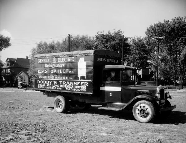 Men are sitting in the cab of a truck owned by Dobby's Transfer, a local and long distance moving company. A sign on the truck advertises General Electric Refrigerators, D.S. Stophlet Inc., Distributors.