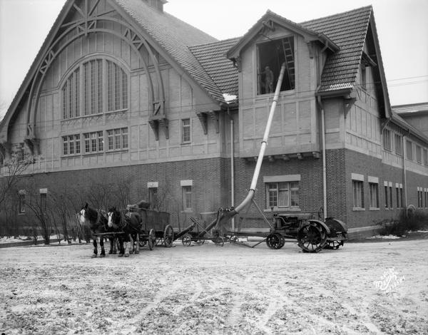 A cargo of oats is unloaded from a horse-drawn wagon with the assistance from a tractor, via a grain elevator at the Stock Pavilion on the University of Wisconsin-Madison campus.