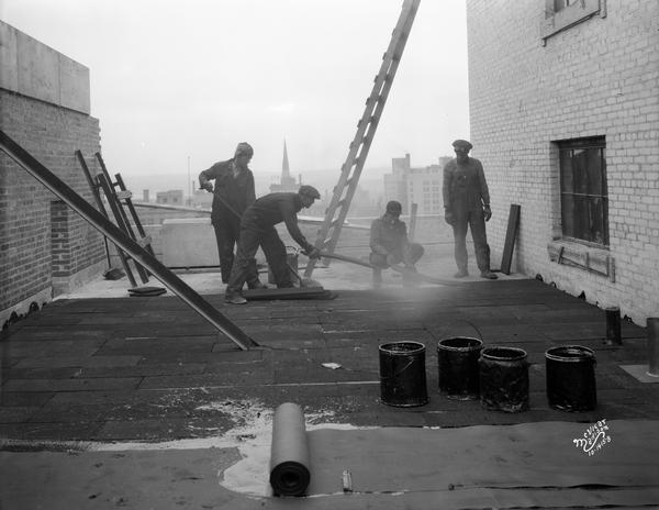 Four men laying Novoid Corkboard on the roof of the Tenney Building, located at 110 East Main Street.