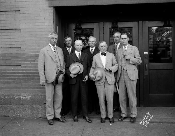 Members of the Progressive Republican Alfred E. Smith For President Club, holding their hats while posing in front of the Park Hotel, 22 South Carroll Street. From left to right: Dr. Adolf Gundersen, George A. Nelson, Fred A. Bachman, John E. Cashman, Dr. W.C. Sullivan, Hugo Meuhrske, Col. Frank W. Kuehl.