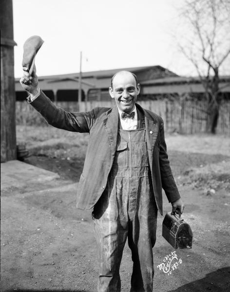A man wearing overalls and a bow tie and carrying a lunchbox is waving his cap, as part of the "You know me Al" presidential campaign of Alfred E. Smith. This image was commissioned by Mr. Stromer of the Progressive Republican Headquarters and the Progressive Republican Alfred E. Smith for President Club.