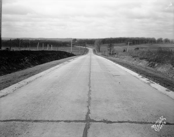 A stretch of paved rural highway winding into the distance features a proprietary centerline joint.