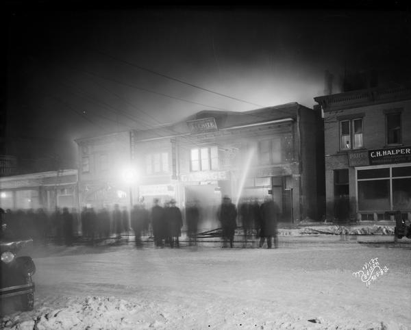 Flames light up the night as fire fighters hose down the Jeffery Brothers Automobile Preparing and Storage building at 621 University Avenue in an attempt to douse the fire, while spectators watch.