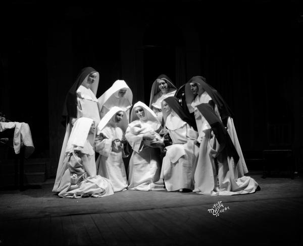 Actresses in nuns' habit costumes from the University of Wisconsin theatre production "The Cradle Song" gather around one nun holding an infant.