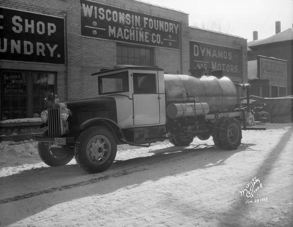 A tank truck that sprays road oil is parked in front of Wisconsin Foundry & Machine Company, located at 613-629 East Main Street.