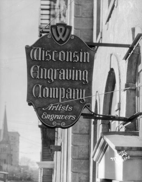 A sign for the Wisconsin Engraving Company, 109 S. Carroll Street, hanging over the sidewalk.
