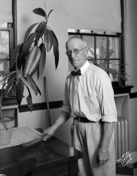 Portrait of Charles H. Seals, janitor at the Security State Bank, 1965 Atwood Avenue. He is standing next to a rubber tree plant and is cleaning the table.
