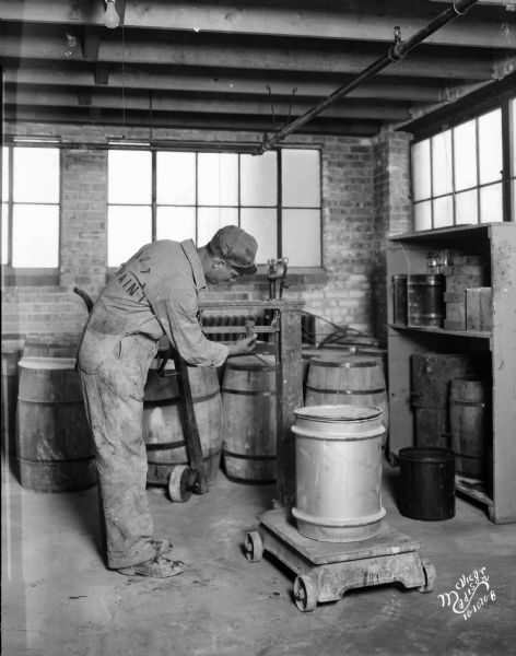 Man weighing a container on an old scale at the Mautz Paint Company.