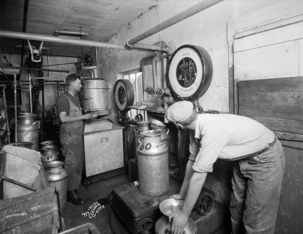 Two men weighing milk cans on Toledo scales at the Pet Milk Company.