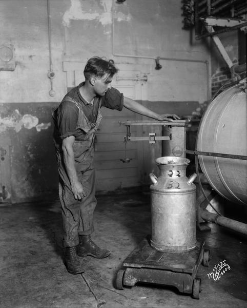 A man weighing a milk can on an old scale at the Pet Milk Company.