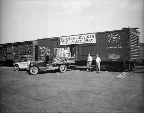 Men unloading Frigidaire refrigerators from New York Central/Cincinnati Northern railroad box car to truck. The delivery is for the Gay Brothers Apartments located on Main street.