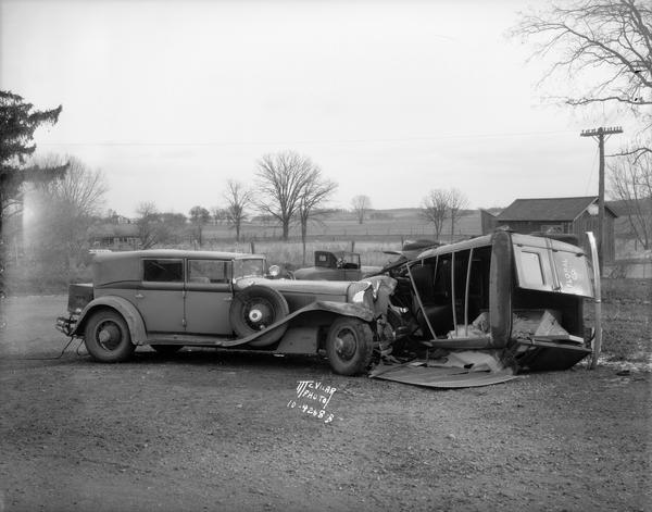 Frank Lloyd Wright's 1929 L29 Cord Phaeton automobile and an overturned Choles Floral Company delivery truck, driven by Frost Choles, at an accident scene at Lakeview north of Oregon, corner of Lakeview Road Highway B and Oregon Road Highway MM. The view also contains a sign pointing to Lake Waubesa and Angus McVicar's automobile in the background.