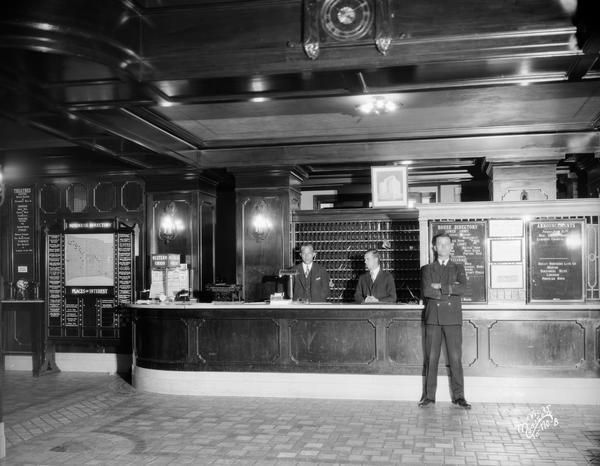 Hotel Loraine lobby registration desk, with three male employees, local business directory, typewriter and Western Union sign.
