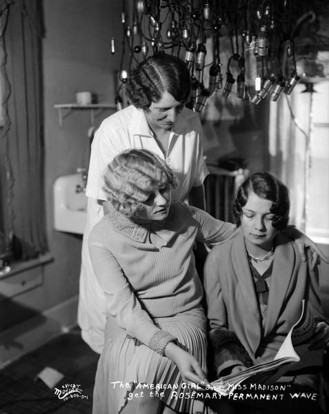 Three women looking at <i>The American Hairdresser</i> magazine in the Rosemary Beauty Shop, located at 521 State Street. The caption reads: "The "American Girl" (Miss Leeds) and "Miss Madison" (Miss Rosenthal / Rosenfeldt) get the Rosemary permanent wave."