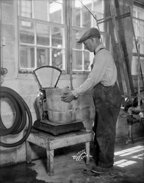 A man is weighing a bucket on an old scale at the Evans Creamery.