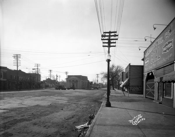 Schenk's Corners, with the Security State Bank, located at Atwood Avenue and Winnebago Street. On the right hand side of the view is Hausmann Fuel Company, 1980 Atwood Avenue and East Side Family Store, 1960 Atwood Avenue. On the left hand side of the view is Palace Theater, 1953 Winnebago; Rennebohm Drug Store, 1957 Winnebago; Harry Hall groceries, 1963 Winnebago; Ed Lynch men's clothing store, 1965 Winnebago; Ed Clements barber, 1969 Winnebago; Universal Grocery, 2001 Atwoos; and Olaf Strand bakery, 2007 Atwood.