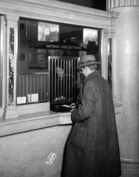 Male customer at savings collection window, Bank of Wisconsin, located at 1 West Main Street. A woman is standing behind the window.