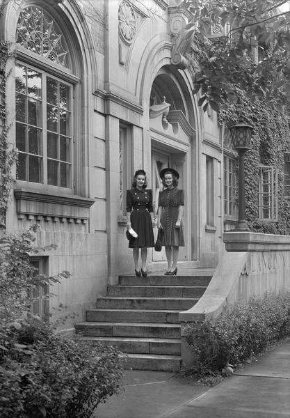 Two Manchester's Department Store coed models, wearing dresses, hats and purses, posing on the steps of Langdon Hall, 633 Langdon Street.