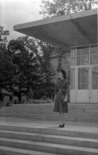 Manchester's Department Store coed model, wearing dress, hat and purse, poses beside the Memorial Union on University of Wisconsin-Madison campus.
