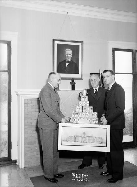 Roy Bergengren, Earl Rentfro and another man holding display of bank cans with Phillips 66 labels.