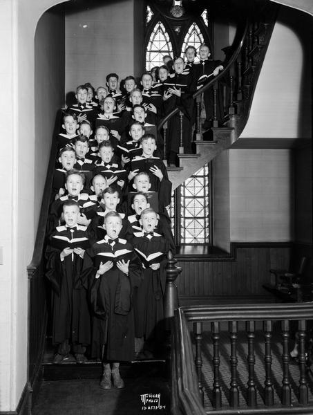 Group portrait of Boys Choir wearing choir robes, holding song books and singing on stairs at the First Methodist Church, located at 203 Wisconsin Avenue.