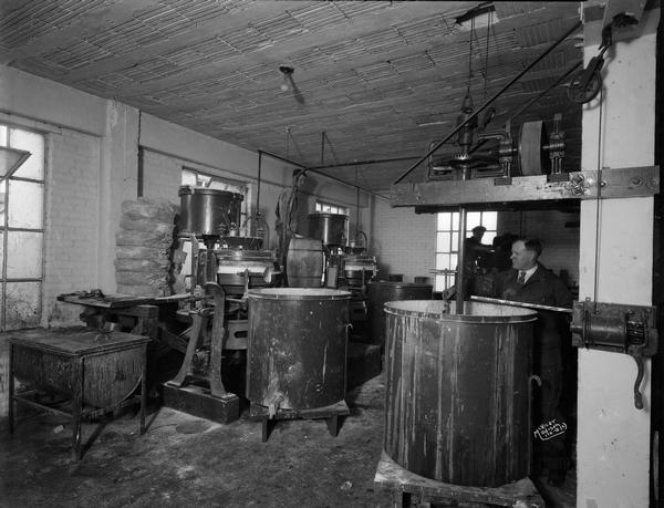 Workers in the mixing room, with mixers running, at Mautz Paint and Glass Company. There are bins and other accoutrements used in the manufacture of paint in the room.