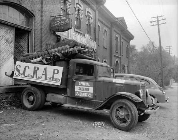 CUNA (Credit Union National Association) truck with load of scrap at Malt House, 1603 Sherman Avenue, at the Yahara River bridge. Sign on side of truck: "SCRAP See CUNA Rap Axis Powers." On truck door: "Official Salvage Depot." Signs on Malt House: "Coca-Cola - Malt House - Coca-Cola;" also, "Fauerbach, Since 1848."