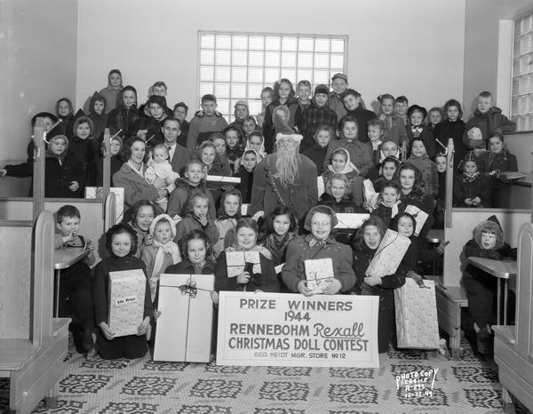 Group portrait of children and a few adults, dressed in coats and hats, posed with a man dressed as Santa Claus, at Rennebohms Drugstore #12, 2526 Monroe Street. The children are prize winners of the Rennebohm Rexall 1944 Christmas doll contest.