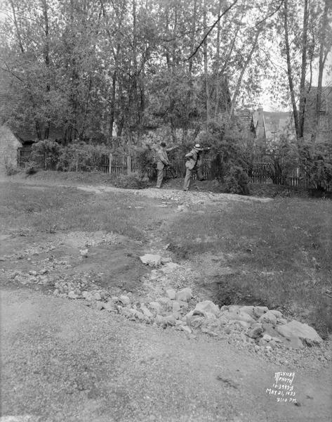Two men examine a break in the dike and the wash out damage at Forest Hill Cemetery, Section 22. The house in the background is located at 454 Virginia Terrace.