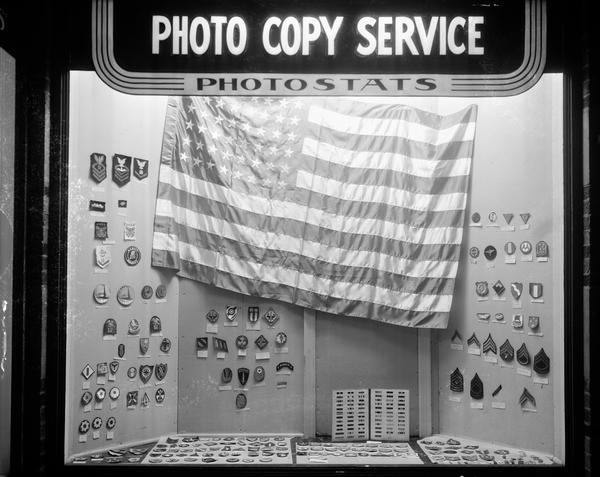 Malcolm McVicar's military insignia collection on display, with a United States flag, in the window of Photo Copy Service shop, 211 West Mifflin Street.
