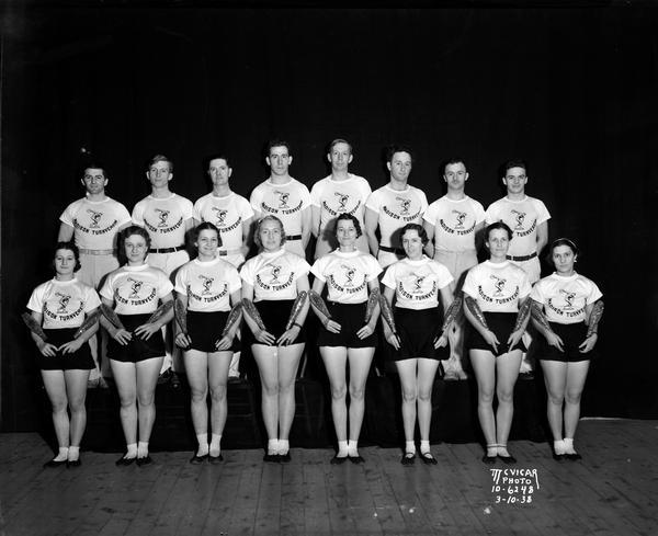 Group portrait of 8 female and 8 male athletes, members of the Madison Turnverein, dressed in shorts and t-shirts. The women are holding Indian clubs in their arms.