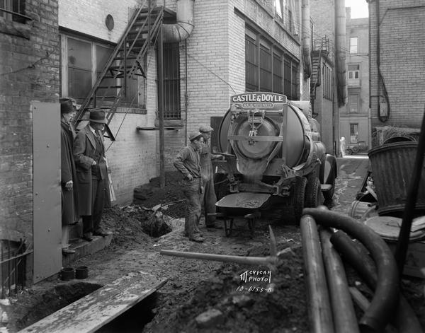 Castle & Doyle Rex Moto Mixer truck delivering ready mixed concrete in the alley behind Dean Clinic, 113-115 N. Carroll Street, with five men looking on.