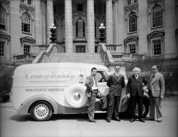 Four men standing next to an Iron Country Liquor Co. truck parked in front of the Wisconsin State Capitol. The sign on the side of the truck reads: "Cream of Kentucky straight bourbon whiskey."