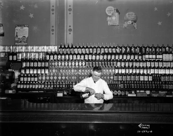 Albert Higgins pouring whiskey behind the bar, with a large display of whiskey bottles behind him at Camel's Tavern, located at 619 University Avenue.