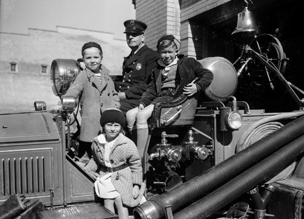 Three children and a fireman sitting on a fire truck.