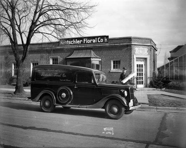 Man holding long stem rose box beside Rentschler Floral Co. delivery truck. He is parked in front of Rentschler greenhouse office building, located at 2500 Regent Street.