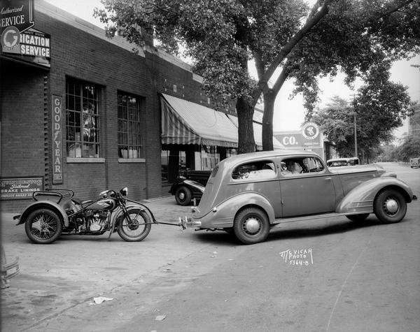 A car pulling service towing a motorcycle in front of Waters Motor's Company, located at 802 East Washington Avenue.