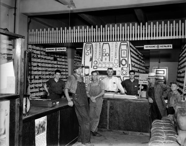 Interior of Niglis Implement Store, an International Harvester dealership located at 724 Williamson Street, with four customers and three employees standing at the counter.