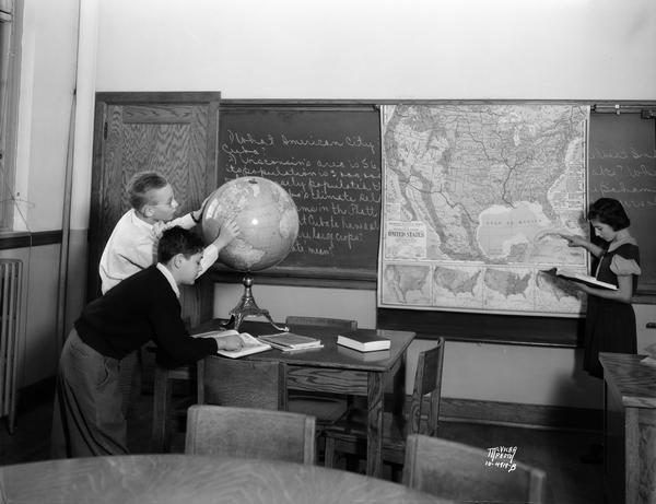 Three West Junior High School students studying a United States map and a world globe.