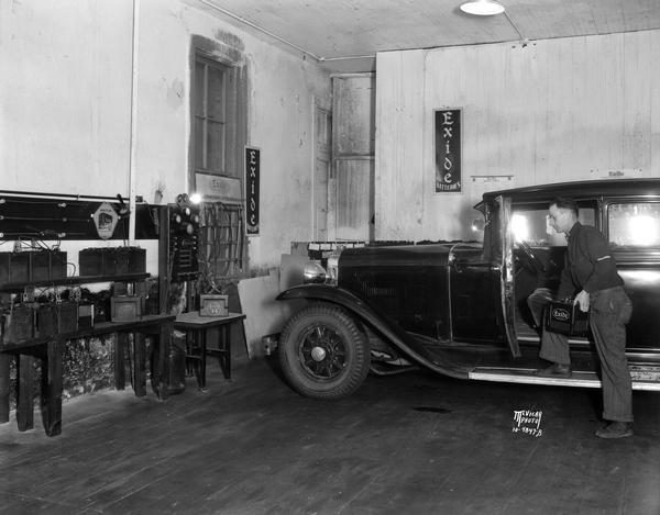 Interior of Harper Battery Service, located at 124 West Main Street. There is a man standing with his foot on the running board of an automobile, holding an Exide battery.
