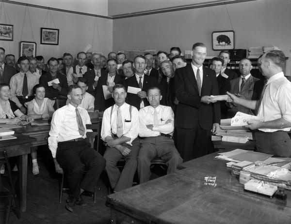 Large group of Dane County farmers, standing in the Dane County Agent's office, holding checks. They are surrounding Floyd Stubley.