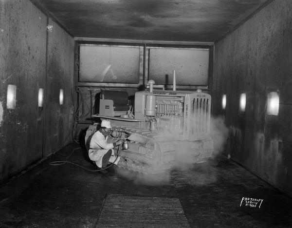 Paint spray booth at Nagle-Hart Tractor & Equipment Company, 754 East Washington Avenue. View shows man spraypainting a Caterpillar tractor.