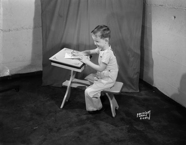 Little boy at child's training desk with bench seat.