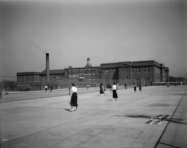 Girls playing tennis on the new West High tennis courts. Includes a full view of the back of West High School.