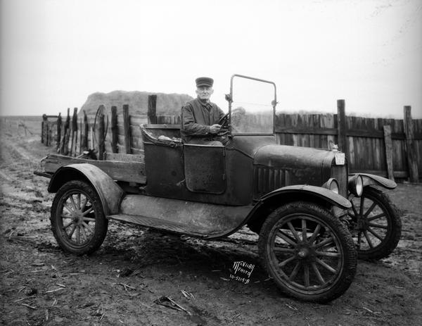 1915 model Ford truck, with driver, in a farm yard.