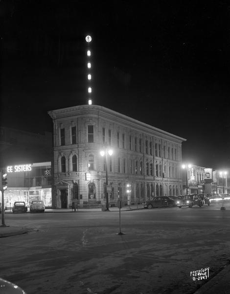 American Exchange Bank, 1 North Pinckney, corner of North Pinckney and East Washington Avenue, a night photograph showing a lighted weather tower, United Weather Tower Incorporated. Other buildings in view are: The Three Sisters, 5 North Pinckney Street; Club Royal, 112 East Washington Avenue; Blied Incorporated Printers, 114 East Washington Avenue; Rocheleau Restaurant, 116 East Washington Avenue; Vital Foods (health food) and Jack's Chicken House, 120 East Washington Avenue; and Blied Office Supplies, 122 East Washington Avenue.