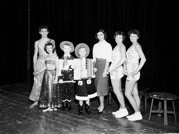 Seven Catholic War Veterans talent show winners (?), including two female baton twirlers, boy and girl with accordion in cowboy dress and boy and girl dancers in harem costumes.