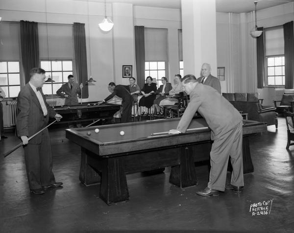 Five men employees play pool in the Pioneer Lounge, Wisconsin Telephone Company, 122 West Main Street, with four women observing.