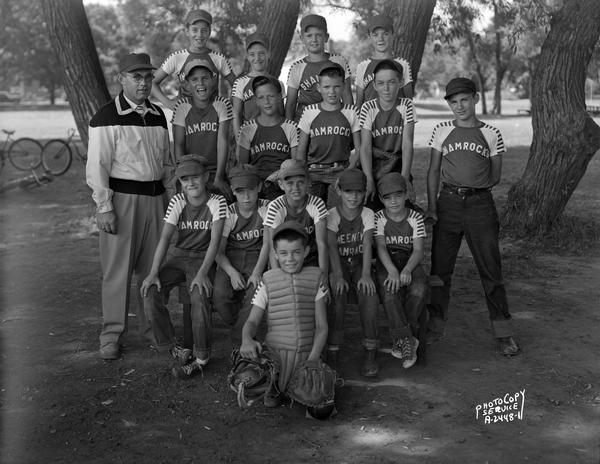 Group portrait of the Shamrock youth baseball team. 15 boys are in Shamrock t-shirts, and one coach is standing on the left.